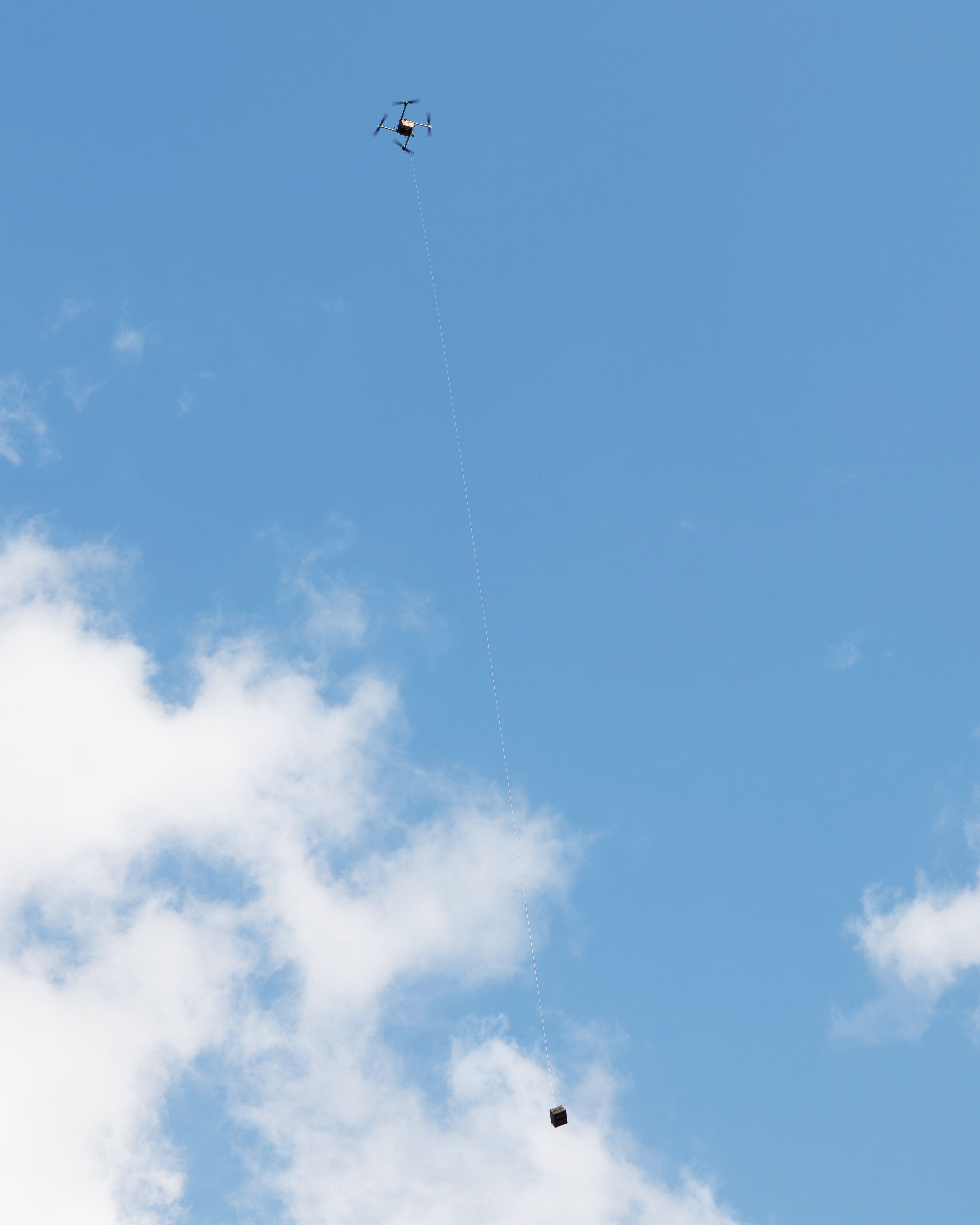 Aircraft above, tether mid-frame, medical payload lowering to the scene